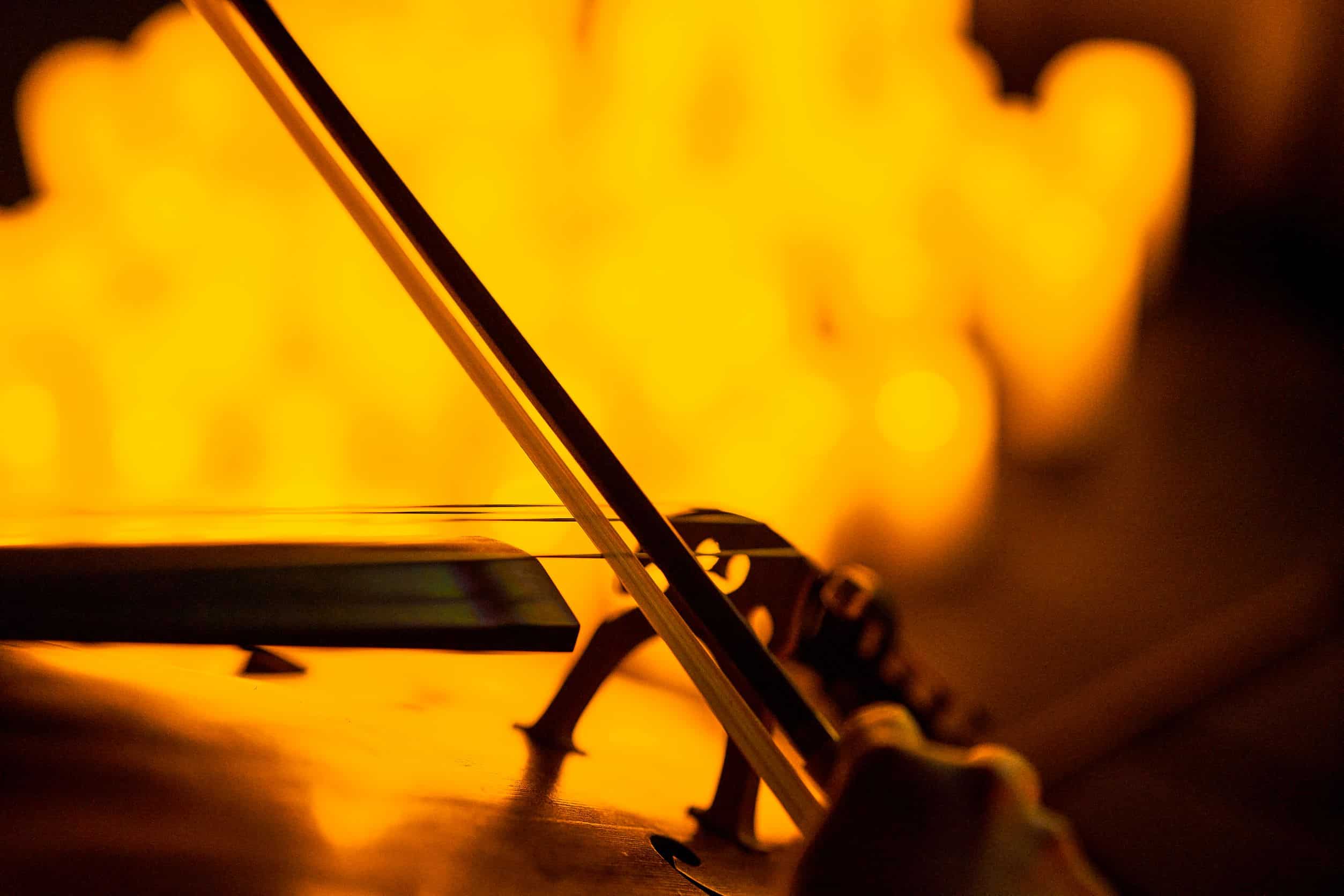 A close-up of a bow being used to play a string instrument with the blurred image of candles in the background.