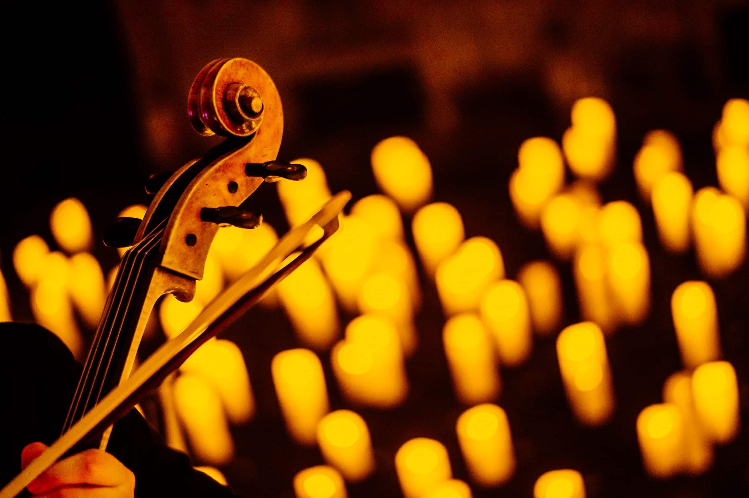 A close-up of the top of a violin and its bow with the glow of candles in the background. 