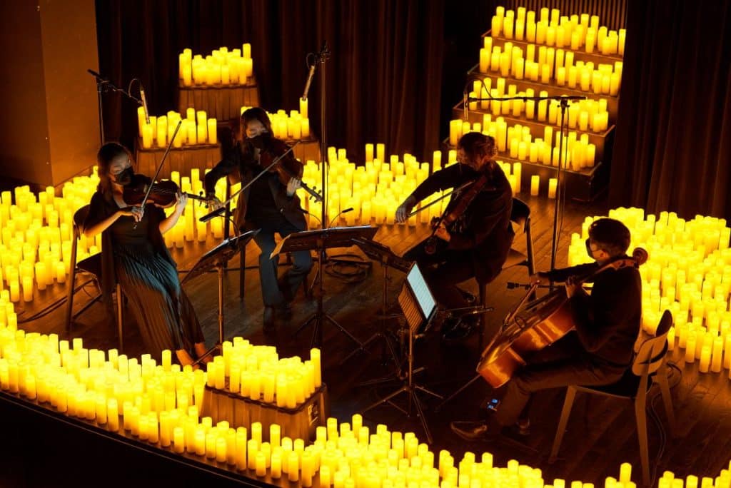 A string quartet performing on a stage covered in candles.