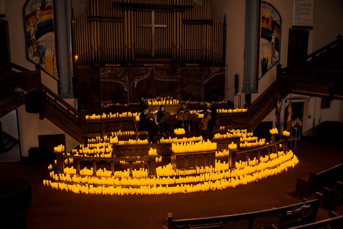 A string quartet performing on a candlelit stage at the Metropolitan Community Church of Toronto