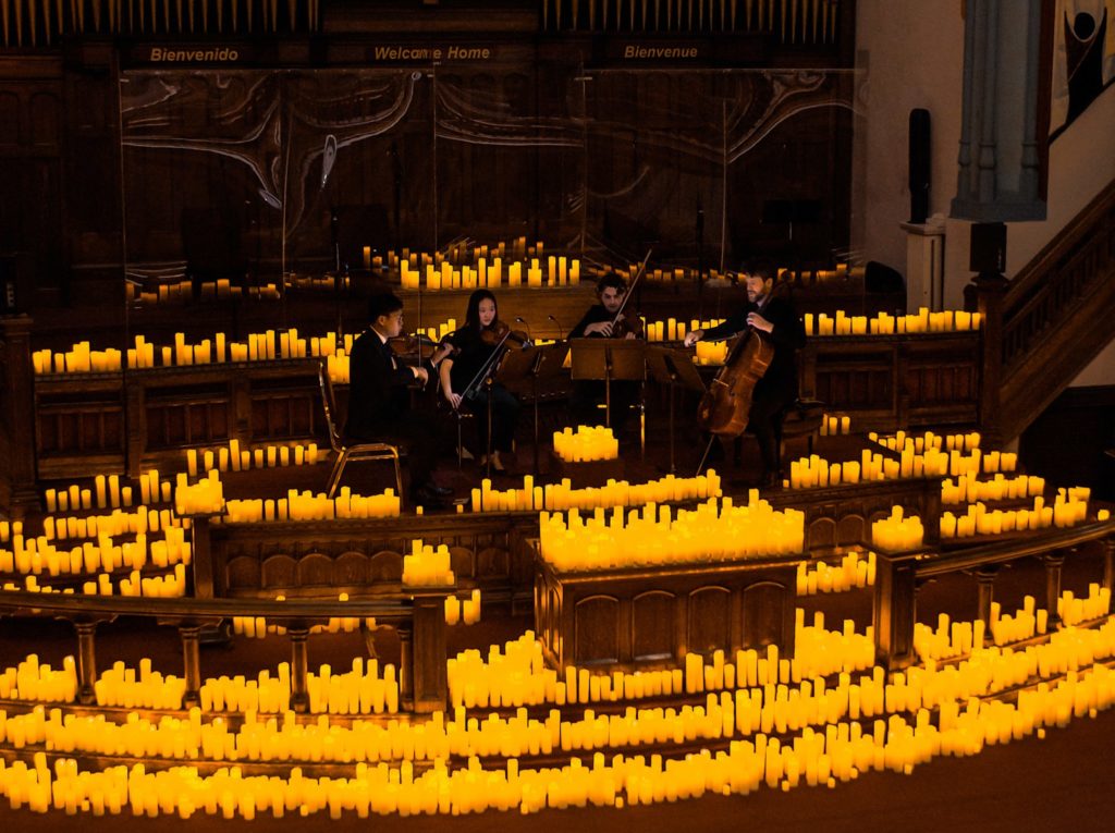 A string quartet performing on stage at Candllelight concert surrounded by hundreds of candles at the altar in the Metropolitan Community Church of Toronto.