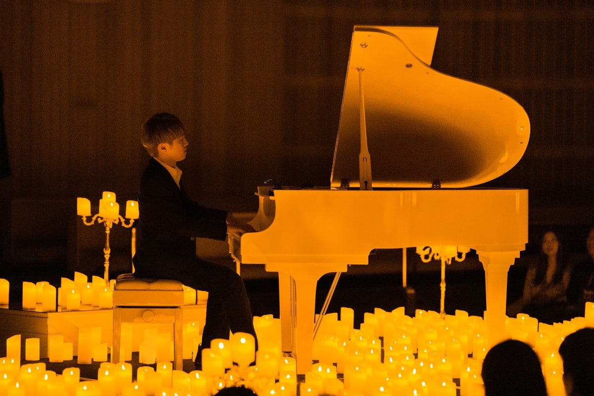 A musician playing the piano with countless candles flickering under it