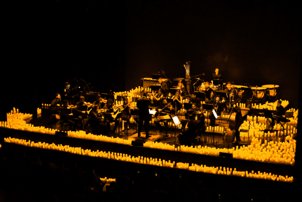 An orchestra performing on a stage surrounded by hundreds of candles.
